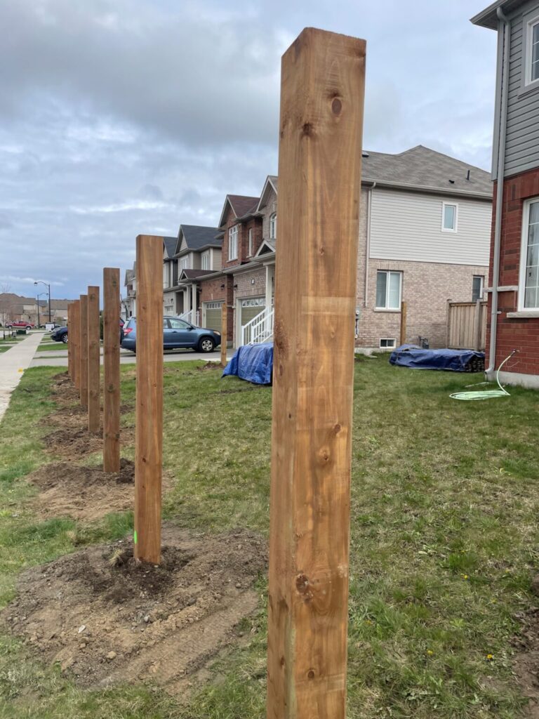 Wooden fence post being installed with concrete in a backyard in Innisfil, Ontario by Post Holes Plus.